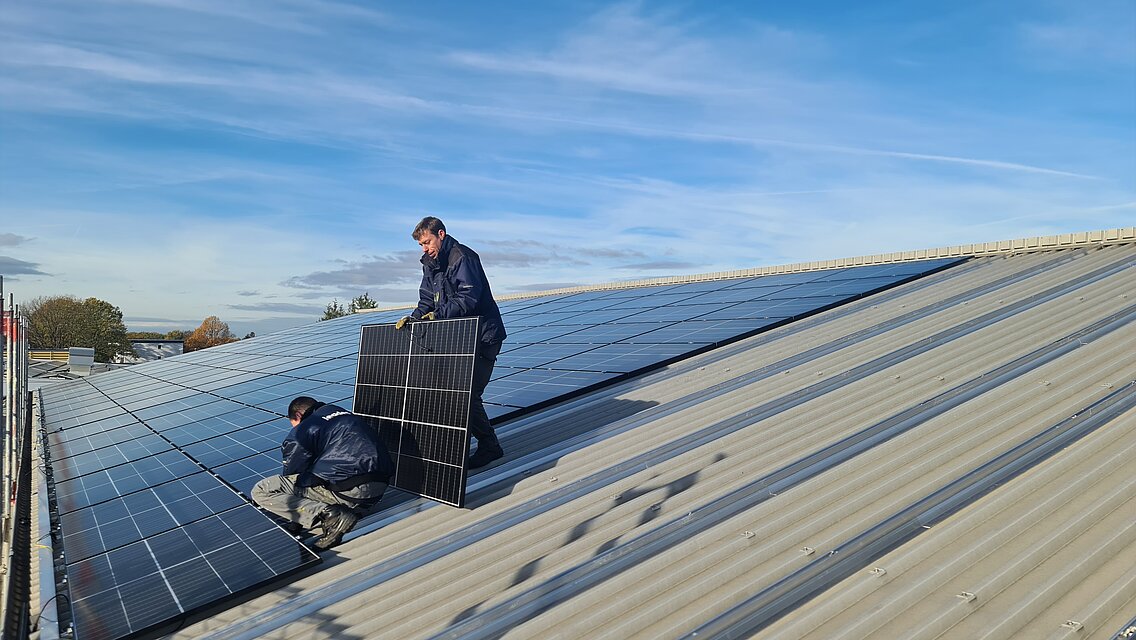 Two men are working on a photovoltaic system on a roof. 