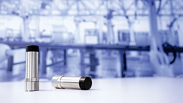 Zwei Vibrationssensoren vor einem unscharfen Fabrikhintergrund. 