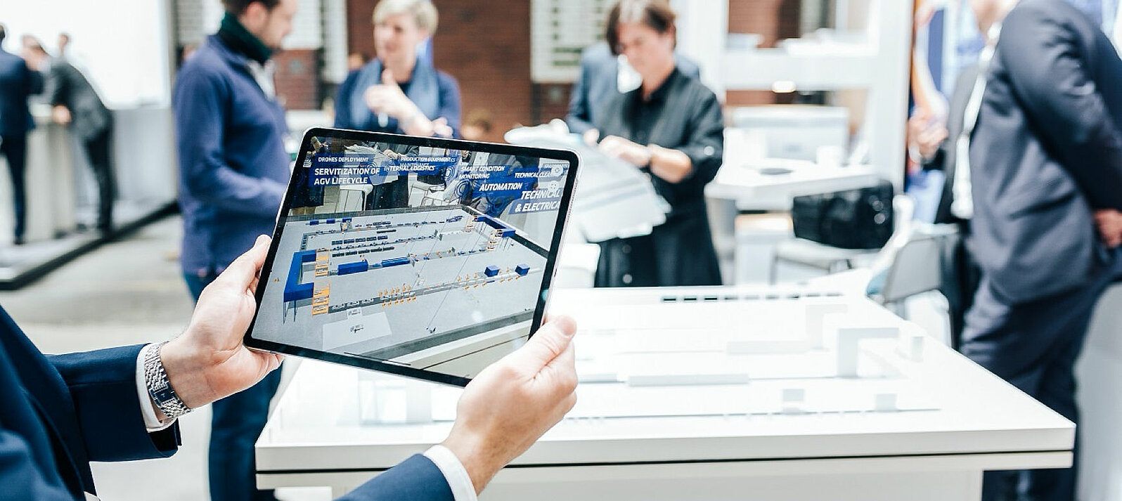 Ein Messebesucher hält ein Tablet in der Hand, auf dem eine digitale Fabrik zu sehen ist.