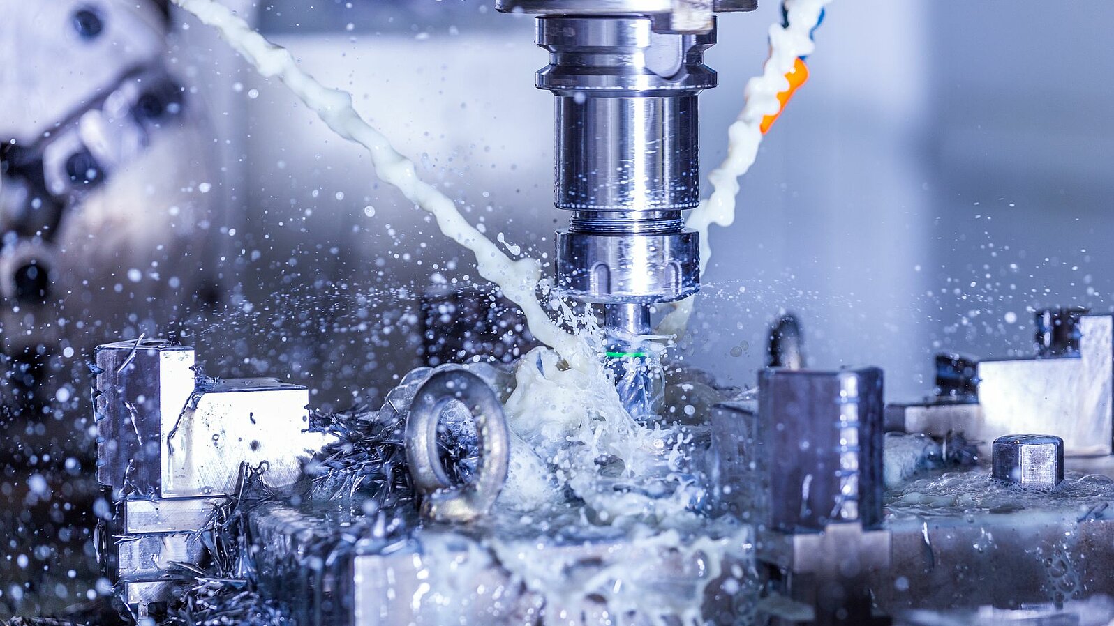 Close-up of CNC steel milling with water coolant streams and splashes.