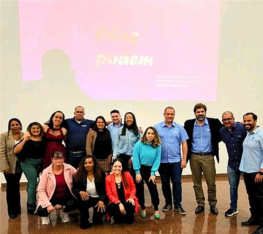 Eine Gruppe verschiedener Personen auf einer Bühne. Im Hintergrund eine rosa Präsentation über Elas Podem.