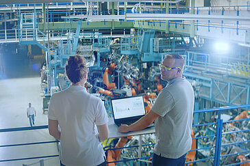 Zwei Personen mit einem Laptop in einer Fabrik.
