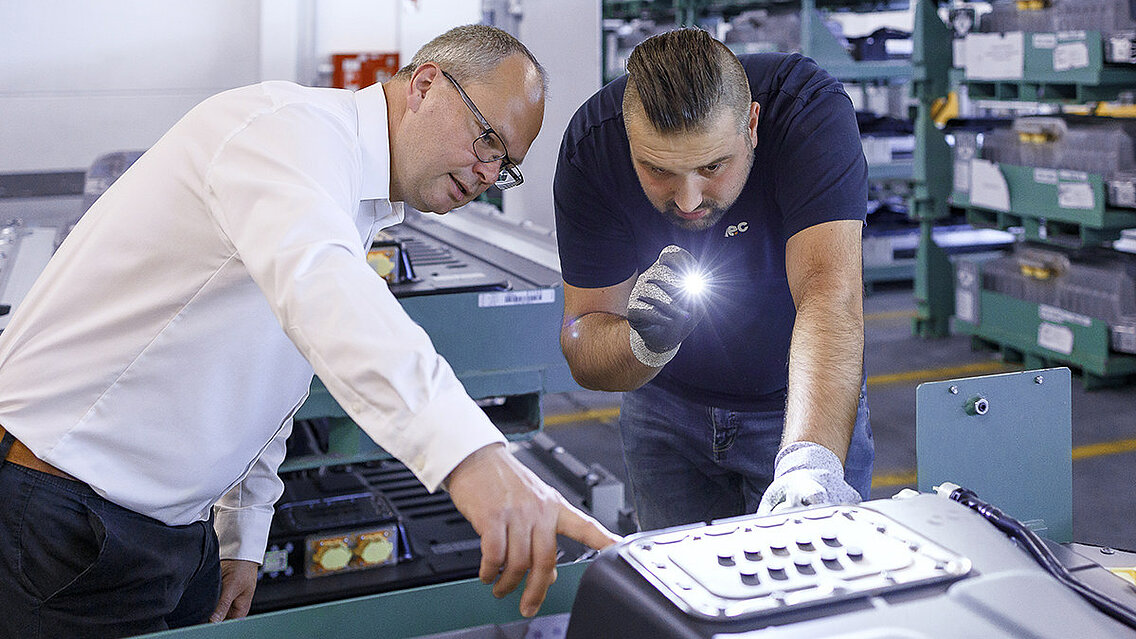 Zwei Leadec-Mitarbeiter überprüfen die Batterie auf einem Gehäuseunterteil.