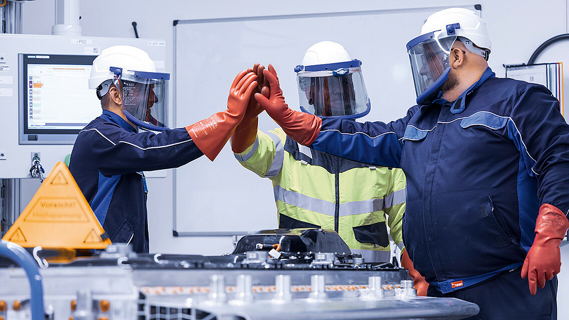 Leadec-Mitarbeitende in Schutzkleidung schlagen ein nach der erfolgreichen Reparatur einer defekten Batterie.