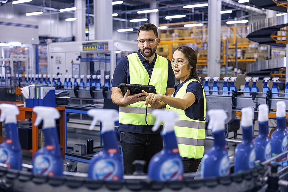 Ein männlicher und ein weiblicher Leadec-Mitarbeiter schauen auf ein Tablet und überwachen die Produktion von Reinigungsmitteln.