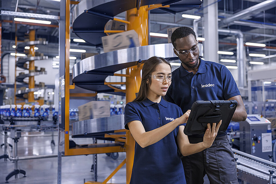 Ein männlicher und ein weiblicher Leadec-Mitarbeiter schauen auf ein Tablet und überwachen die Produktion von Reinigungsmitteln.