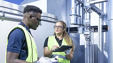 Zwei Leadec-Mitarbeitende mit Tablet an der Lüftungsanlage auf einem Fabrikdach.