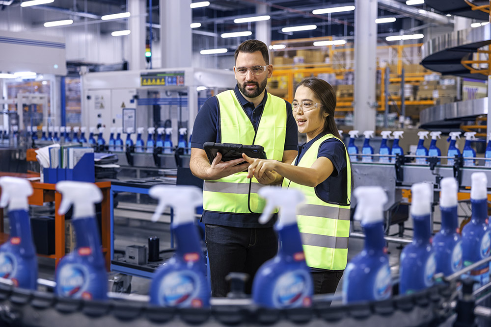 Ein männlicher und ein weiblicher Leadec-Mitarbeiter schauen auf ein Tablet und überwachen die Produktion von Reinigungsmitteln.