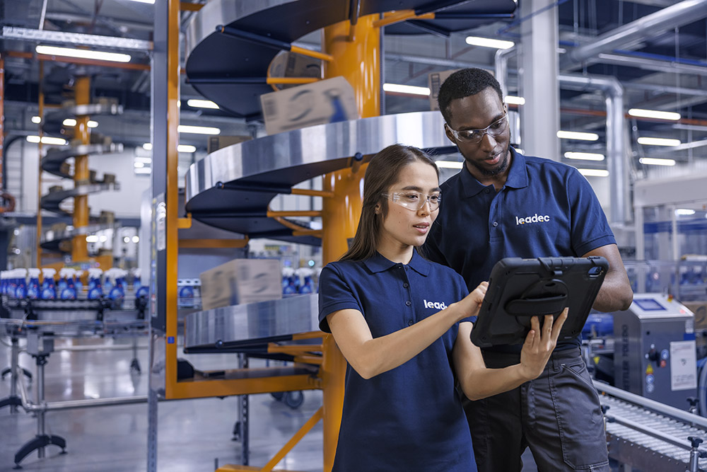 Ein männlicher und ein weiblicher Leadec-Mitarbeiter schauen auf ein Tablet und überwachen die Produktion von Reinigungsmitteln.